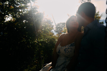 Romantic Couple Sitting on a Swing Outdoors During Golden Hour - Backlit Portrait of Love and...