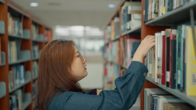 Asian university student wearing glasses searching for books in a university library during intensive study or while working on a thesis or dissertation