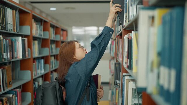 Asian university student wearing glasses searching for books in a university library during intensive study or while working on a thesis or dissertation