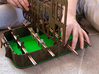 Close-up of adult man hands assembling wooden retro tabletop football game on green base.Concept of...