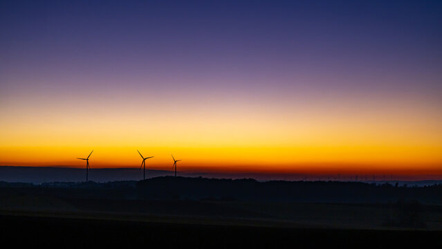 Untergang der Wintersonne mit einem starken Farbverlauf &uuml;ber den gesamten Himmel und Windr&auml;dern im Vordergrund