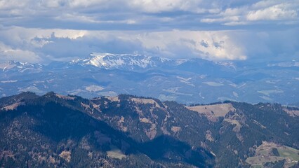 Fototapeta premium Sweeping panoramic view of rugged mountains under partly cloudy blue sky in the Alps.