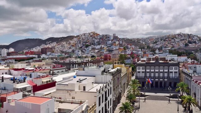 Las Palmas, Gran Canaria, Spain &ndash; Town hall Casas Consistoriales at Plaza Mayor de Santa Ana with palm trees and flags and buildings on the hill