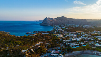 Aerial view of the dramatic coastline meeting the turquoise waters, backed by the rugged mountains of Kolymbia, Rhodes, Greece.
