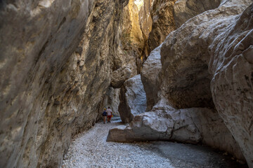 Massive limestone walls of a deep narrow canyon with tiny unrecognizable silhouettes of explorers for scale. Spectacular geological formation in Saklikent National Park. September, Turkey.
