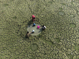 Rajshahi, Bangladesh - 14 April 2024: Aerial view of women collecting water from a scarce puddle in a cracked, parched landscape under the dry season sun.
