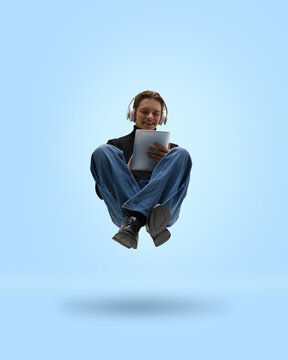 Casual man levitating with tablet and headphones on blue background. Concept of SaaS onboarding, product promo, platform walkthroughs, user education, feature discovery, self paced software learning.