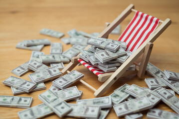 Many US dollar bill banknotes on beach chair and wooden table background. Financial freedom through passive income, success wealth from investment, interest rate from bank account and so on concept.
