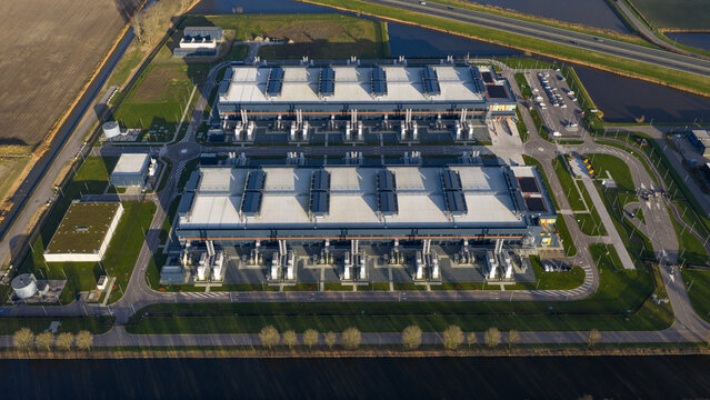 Aerial view of symmetrical data centers gleaming under the soft sunlight, bordered by tranquil canals and roadways, Agriport, Middenmeer, Netherlands.
