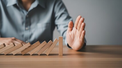 Man stopping falling wooden dominoes with his hand. Risk management and crisis prevention. Business professional intervening to halt a chain reaction and protect stability on a table