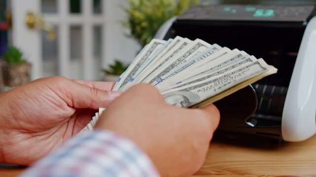 Close Up Of Male Hands Holding Stack Of American Dollar Bills And Feeding Them Into Money Counting Machine. Financial Operations Cash Flow Banking And Investment Theme. 