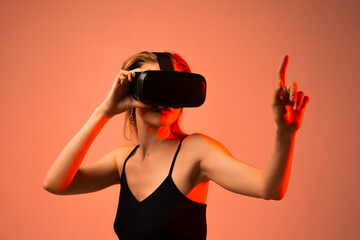 Young woman using virtual reality headset and pointing forward in immersive digital environment with futuristic red lighting