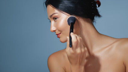 Beautiful Woman Applying Blush With Makeup Brush on Glowing Skin in Studio