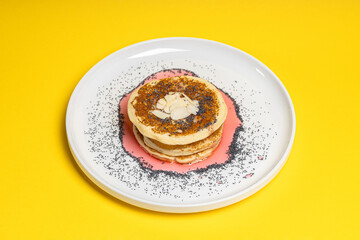 Stack of pancakes with syrup and nuts on yellow background
