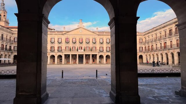 Cinematic panning video shot moving between stone columns at Spain square, also known as Plaza Berria, in Vitoria Gasteiz, revealing historic architecture and an empty urban square in Spain. High