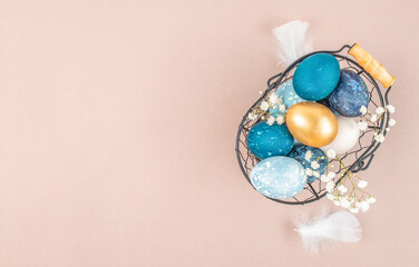 Elegant Easter flat lay with blue and gold eggs in wire basket on pastel background with copy space
