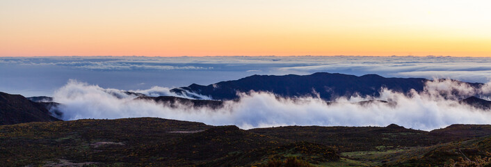 Naklejka premium Dramatic sea of clouds over Madeira's mountains at sunrise. Panoramic view of Portugal's scenic island landscape. Nature's beauty with sunrise colors above the clouds.