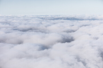 Serene aerial view reveals a dense blanket of white clouds stretching endlessly beneath a pale sky....
