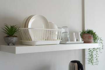 Minimalist white floating shelf in a modern kitchen featuring organized white dishes, glasses, and small decorative potted plants