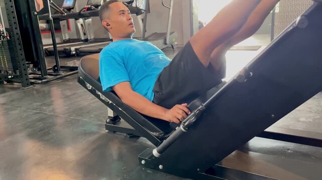 Asian Man Doing Leg Press Exercise on Machine in Gym