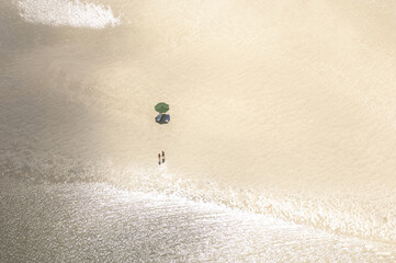 Aerial view of shimmering sand meets the turquoise water, where a solitary umbrella casts a shadow over two figures on the beach, Seychelles.