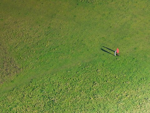 Aerial view of a person stands alone in a field of vibrant green, casting a long shadow under the winter sun, Basingstoke, England, United Kingdom.