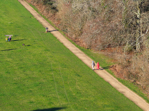 Aerial view of a pathway cutting through vibrant green grass, bordered by trees, with people strolling along, Basingstoke, England, United Kingdom.
