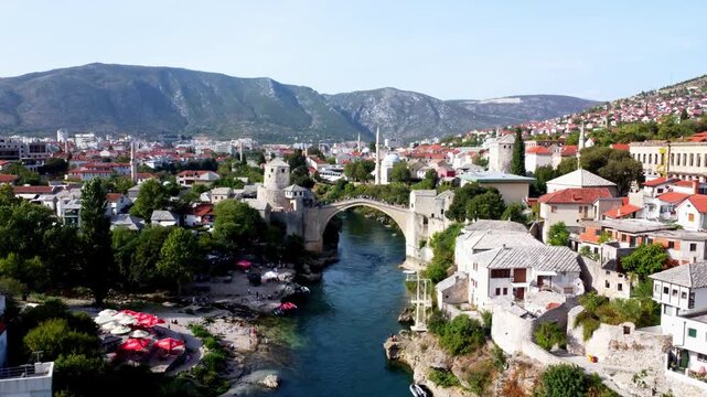 Drone footage of the Old Bridge in Mostar at sunrise, Bosnia and Herzegovina. Aerial view of the historic stone bridge over the Neretva River, ideal for travel and tourism use.