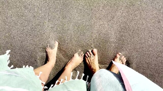 Top view of caucasian couple's feet wriggling toes after wave crash around it