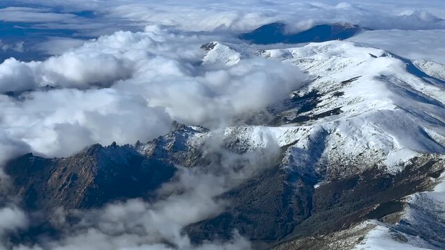 An elevated aerial aerial view of Navacerrada Mountain Range, North of Madrid city, taken from an airplane cockpit, partially covered by snow and some broken low altitude stratus clouds.