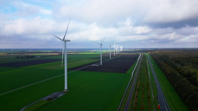 Aerial view of line of white wind turbines extending into distance across green flat fields in Zeewolde Netherlands. Sustainable power generation infrastructure in Dutch polder landscape.