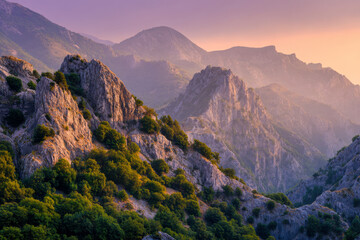 Majestic rugged mountain range covered with lush green trees glowing under the warm light of a soft sunset sky with misty peaks in the background