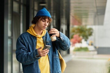 Curly teenager in a blue beanie enjoying coffee outdoors on a cool autumn day