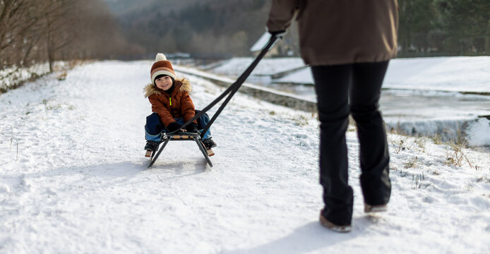 Mother pulls a sled with a happy child in the freezing winter weather