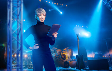 Event manager uses tablet on concert stage with lighting and instruments, coordinating live show...