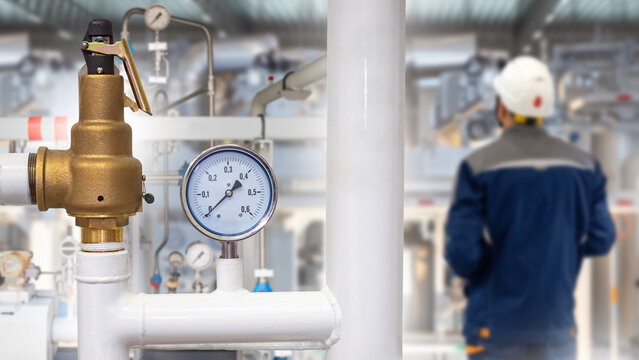 Industrial safety, pressure gauge and relief valve monitor fluid levels in plant pipeline while technician oversees system, supporting equipment protection and process stability.