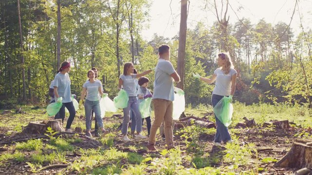 Wide view of volunteer group walking in forest area. Caucasian man and woman holding trash bags. Diverse adults cleaning nature together. Environmental protection action. Protecting nature.