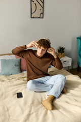 Curly teenager enjoying music while relaxing in a cozy bedroom at home