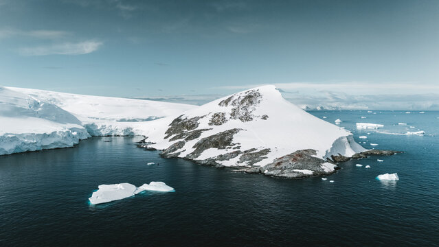 Aerial view of the stark white snow-covered land meeting the dark blue sea, creating a stunning contrast of color and texture, Palaver Point, Antarctica.