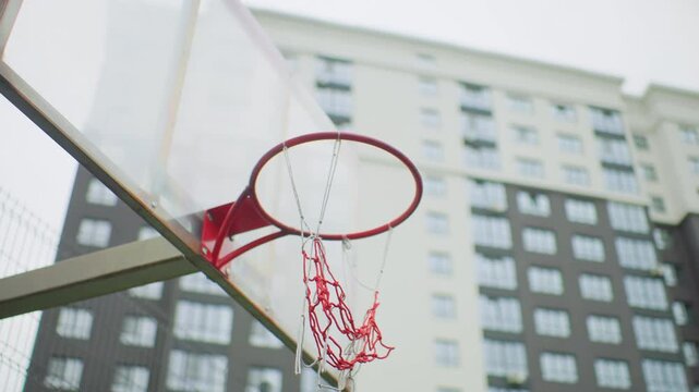 Urban basketball swish above metal hoop, closeup of red rim and nylon net against highrise backdrop, slow motion ball drop capturing triumphant score, pickup game energy, youth player celebration