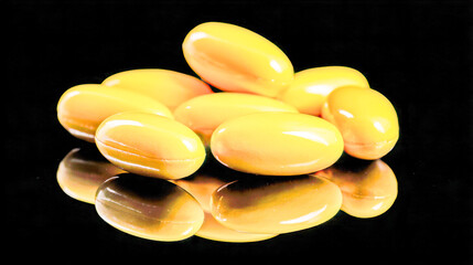 Yellow glossy soft gel capsules reflected on a smooth black surface, symbolizing dietary supplements or vitamins for health and wellness benefits