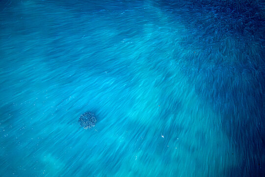 Aerial view of the vibrant turquoise waters swirling around a dark patch, creating an ethereal dance of light and shadow, Peron, Western Australia, Australia.