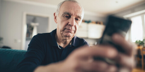 Elderly man using smartphone at home, looking focused and serious, symbolizing technology use, digital communication and aging in the modern world.
