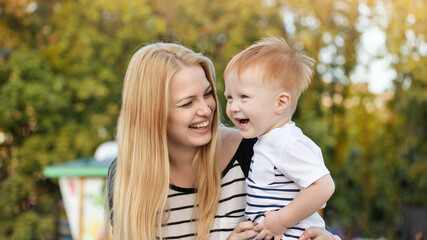 Happy mom and son are hugging and laughing outdoors in the summer. Mother is holding the kid boy in her arms