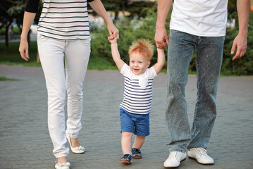 Family is walking outside in the summer in the park. Happy kid boy is taking his first steps and smiling.