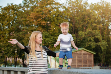 Happy kid boy is taking his first steps and smiling in outdoor. Baby is playing with mother in the park in the summer.