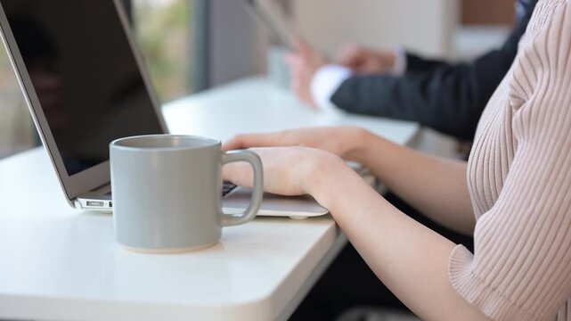 落ち着いたオシャレなカフェやオフィス空間で、ノートパソコンを使う若い女性の手元の顔無しのクローズアップ