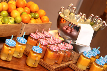 Luxury breakfast buffet featuring fresh fruit smoothies in mason jars with checkered lids, alongside crates of citrus fruits and chilled bottled juices. Elegant lifestyle beverage catering.
