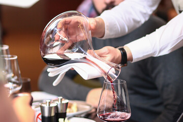 Professional sommelier pouring red wine from a glass decanter for a man at a luxury fine dining restaurant. Elegant lifestyle photography capturing premium wine service and hospitality.