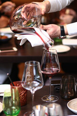 Professional sommelier pouring red wine from a glass decanter for a woman at a luxury fine dining restaurant. Elegant lifestyle photography capturing premium wine service and hospitality.